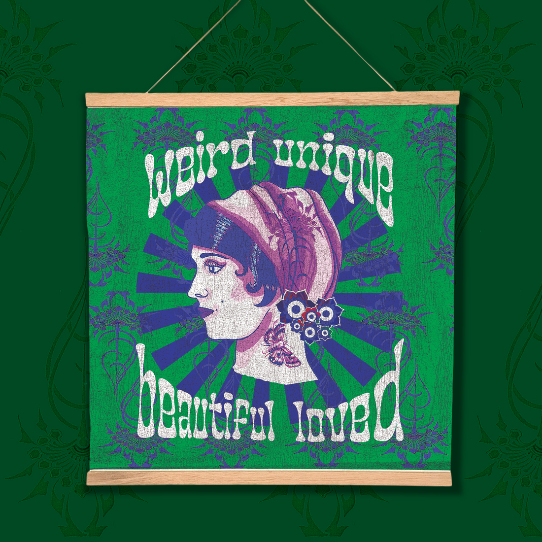A square hanging wall art print with a light wood top and bottom frame, featuring a stylized profile illustration of a woman in a green and cream headscarf on a teal background with decorative text reading 'weird unique beautiful loved.' The piece is shown against a dark teal patterned backdrop.